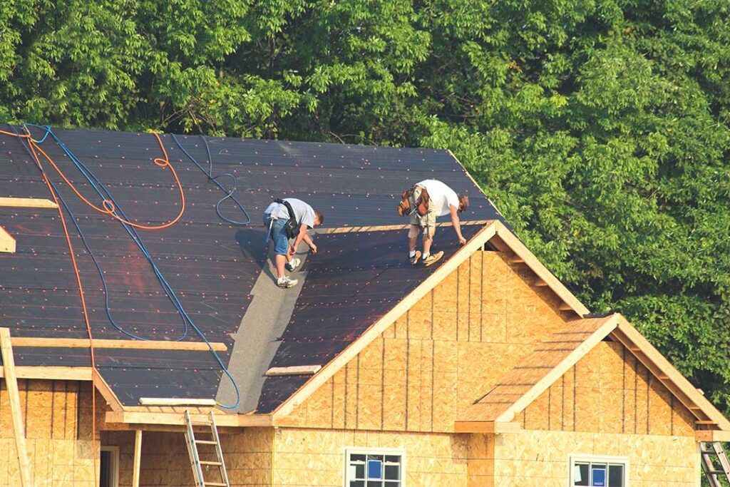 Homeowner viewing curled shingles and roof wear from the ground beside a suburban house.